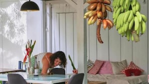A dining area with a table and chairs, a hanging light fixture, and a sofa with cushions. - CASA BOHÖ (Cahuita)