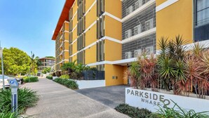 A modern building with a yellow facade, a sign reading "PARKSIDE WHARF," and a parking area with a meter. - Waterfront Sunset Suite: 1 Bed Apt, Sunset Views (Darwin City)