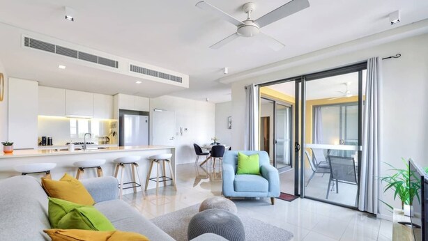 A modern living room with a grey sofa, a blue armchair, and a kitchen in the background. - Waterfront Sunset Suite: 1 Bed Apt, Sunset Views (Darwin City)