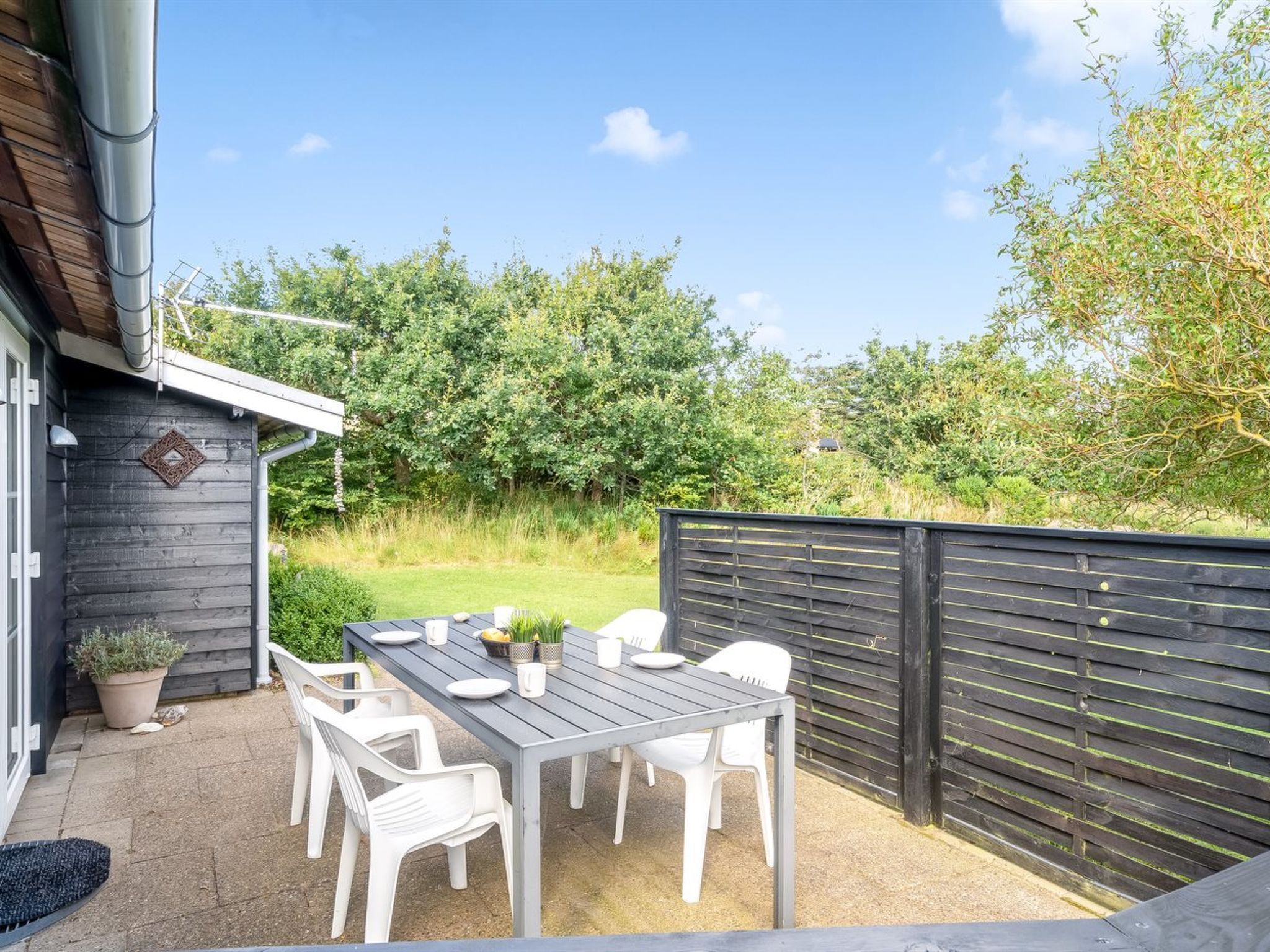 Une terrasse extérieure avec une table et des chaises, entourée d’une clôture en bois et de verdure.