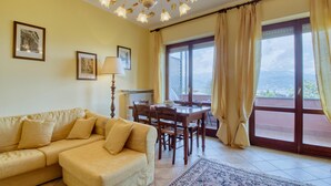Ein gemütliches Wohnzimmer mit einer Couch, einem Esstisch mit Stühlen, einer Lampe und Meerblick durch große Fenster.