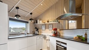 Una cocina moderna con armarios blancos, una campana extractora de acero inoxidable, una batidora de pie roja y un ventanal con vistas a un edificio.