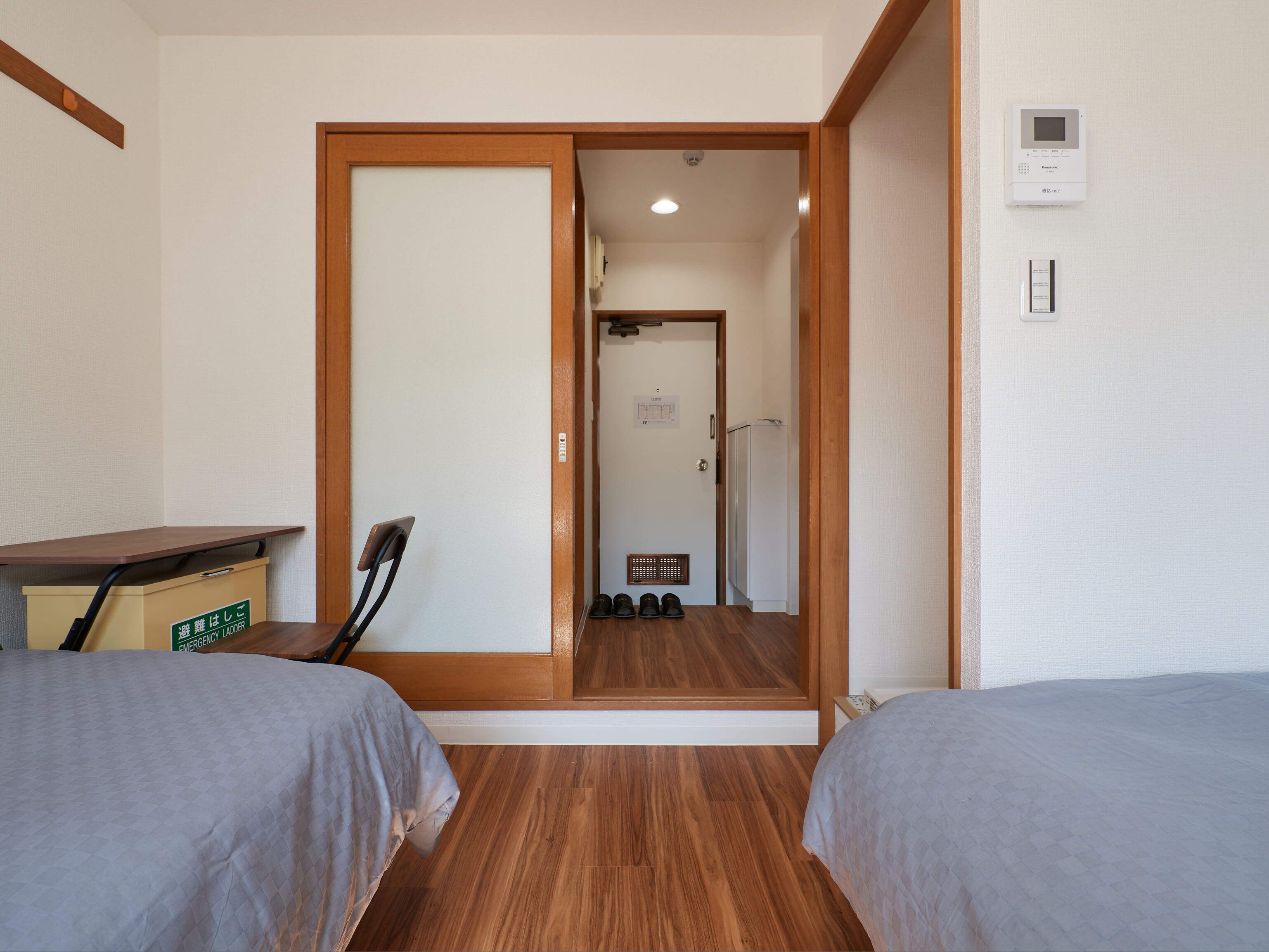 A hotel room with two beds, a wooden floor, a desk, and a shoe rack.