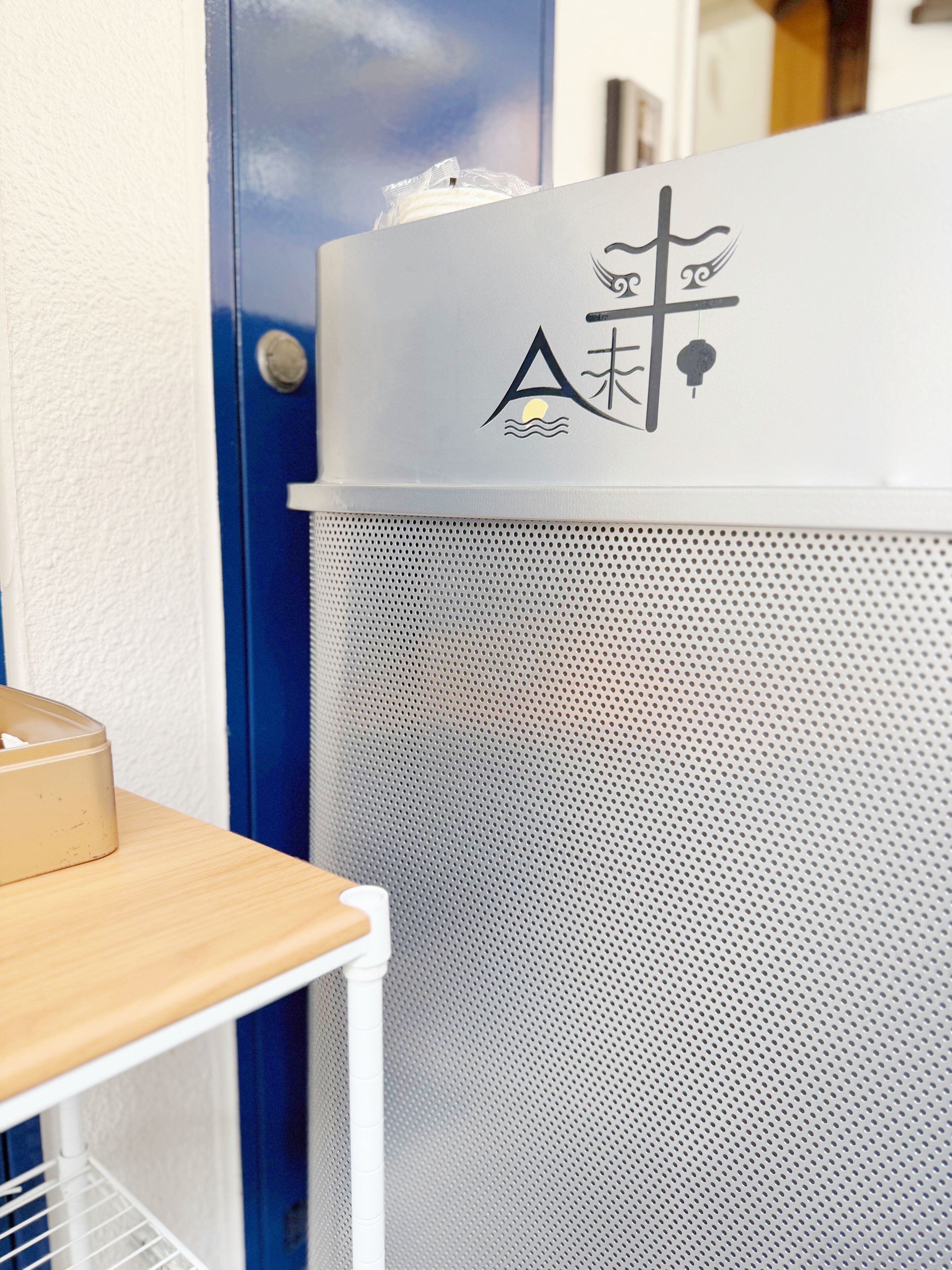 Pared blanca con un panel perforado, una puerta azul y una mesa de madera con una caja.