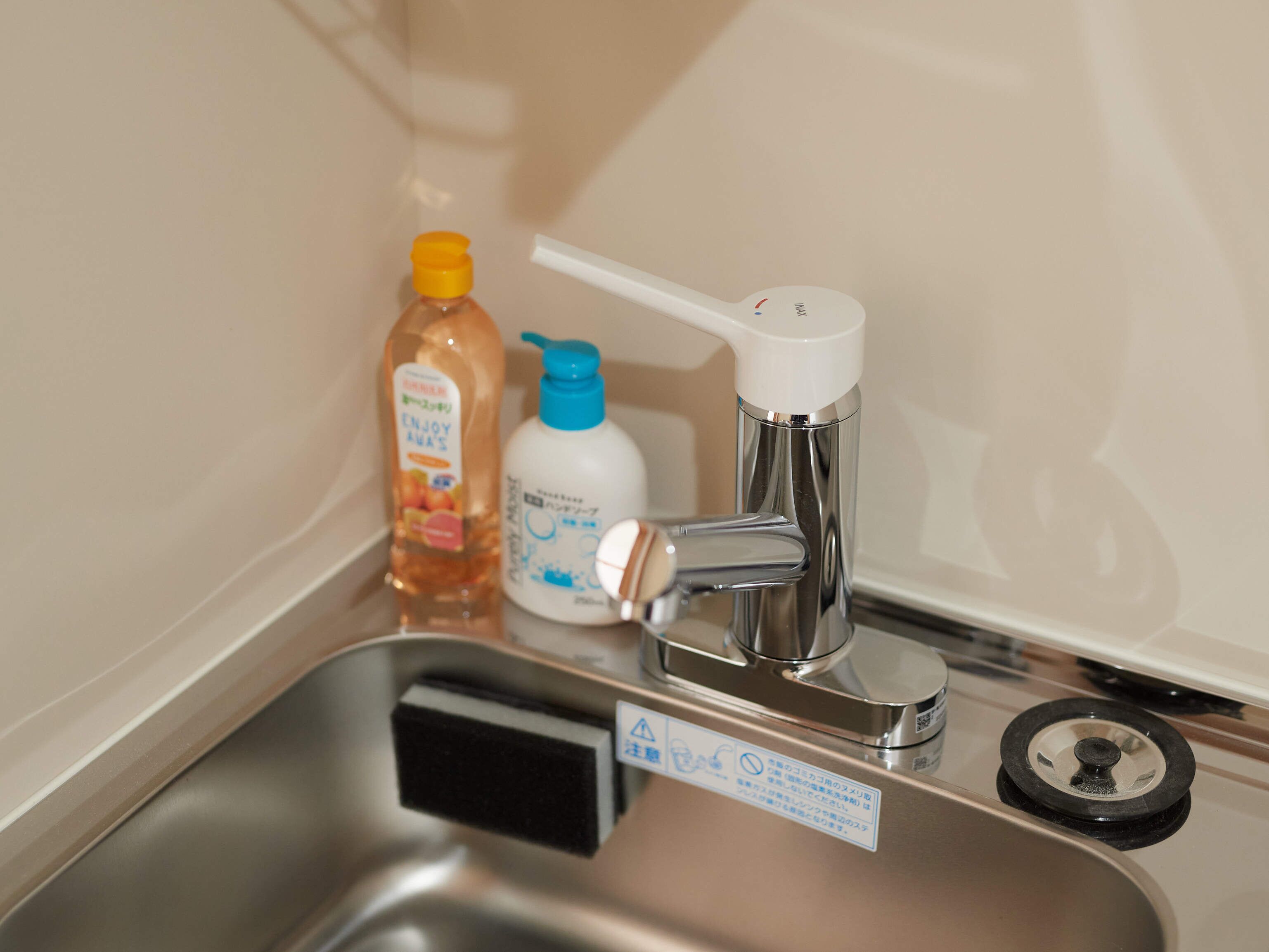 A stainless steel sink with a faucet, two bottles of liquid soap, and a black sponge.