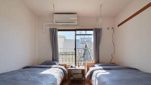 Ein Zimmer mit zwei Betten, einem kleinen Tisch und einem Fenster mit Vorhängen.