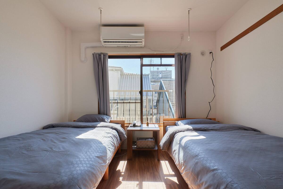 A room with two beds, a small table, and a window with curtains.