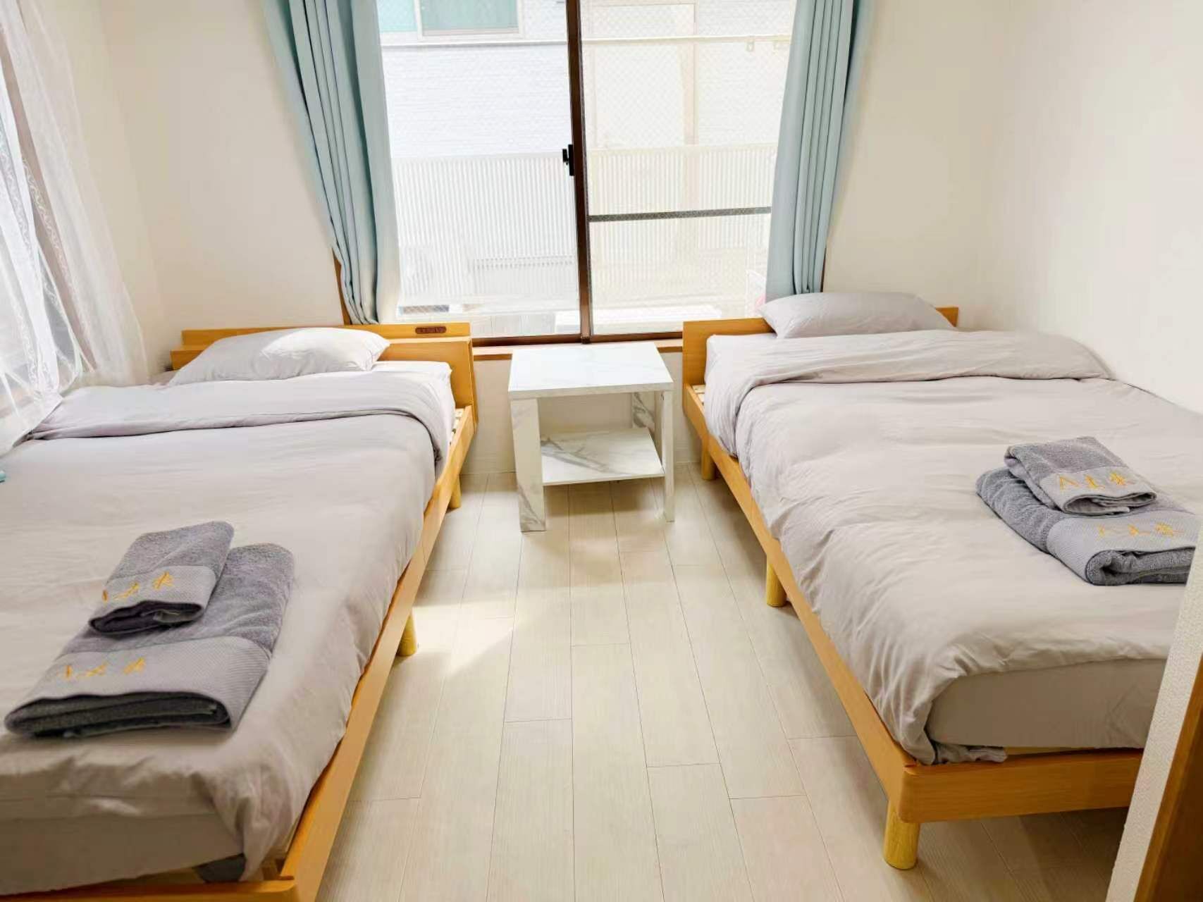 Une chambre d’hôtel avec deux lits simples, une petite table et une fenêtre avec des rideaux.