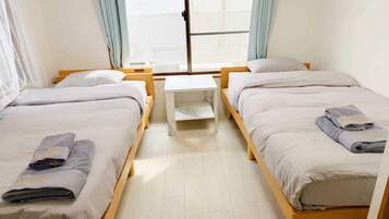 Une chambre d’hôtel avec deux lits simples, une petite table et une fenêtre avec des rideaux.