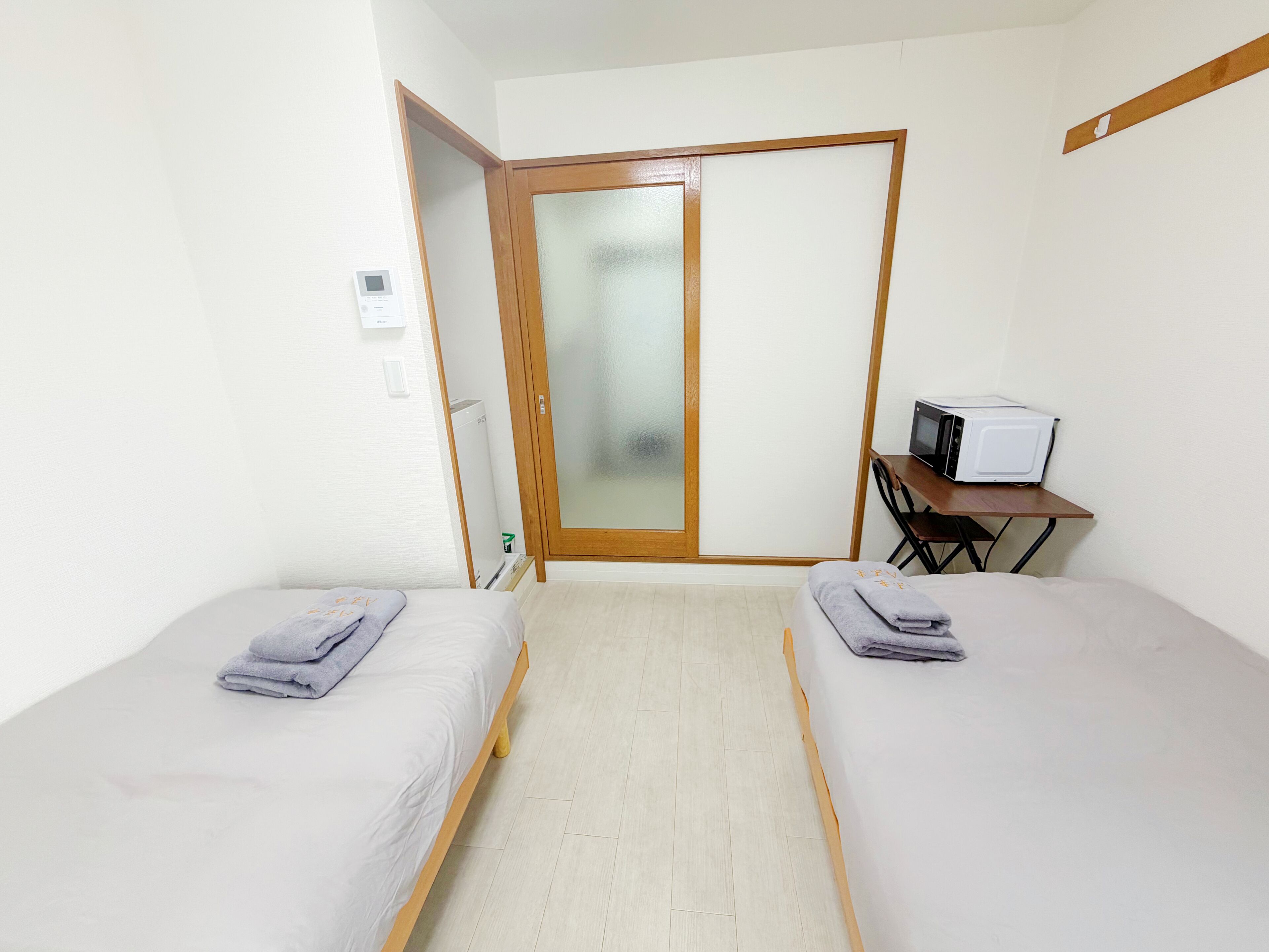 Une chambre avec deux lits, un bureau avec un ordinateur, un four à micro-ondes et une porte-fenêtre coulissante.
