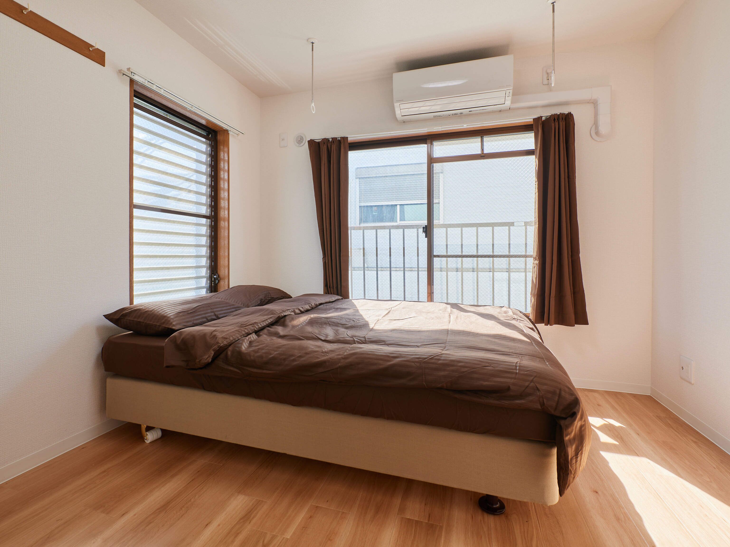 Quarto com cama, janela com cortinas, ar condicionado e piso de madeira.
