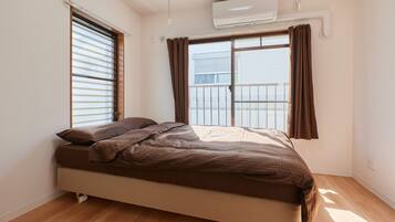 Une chambre avec un lit, une fenêtre avec des rideaux, un appareil de climatisation et un plancher en bois.