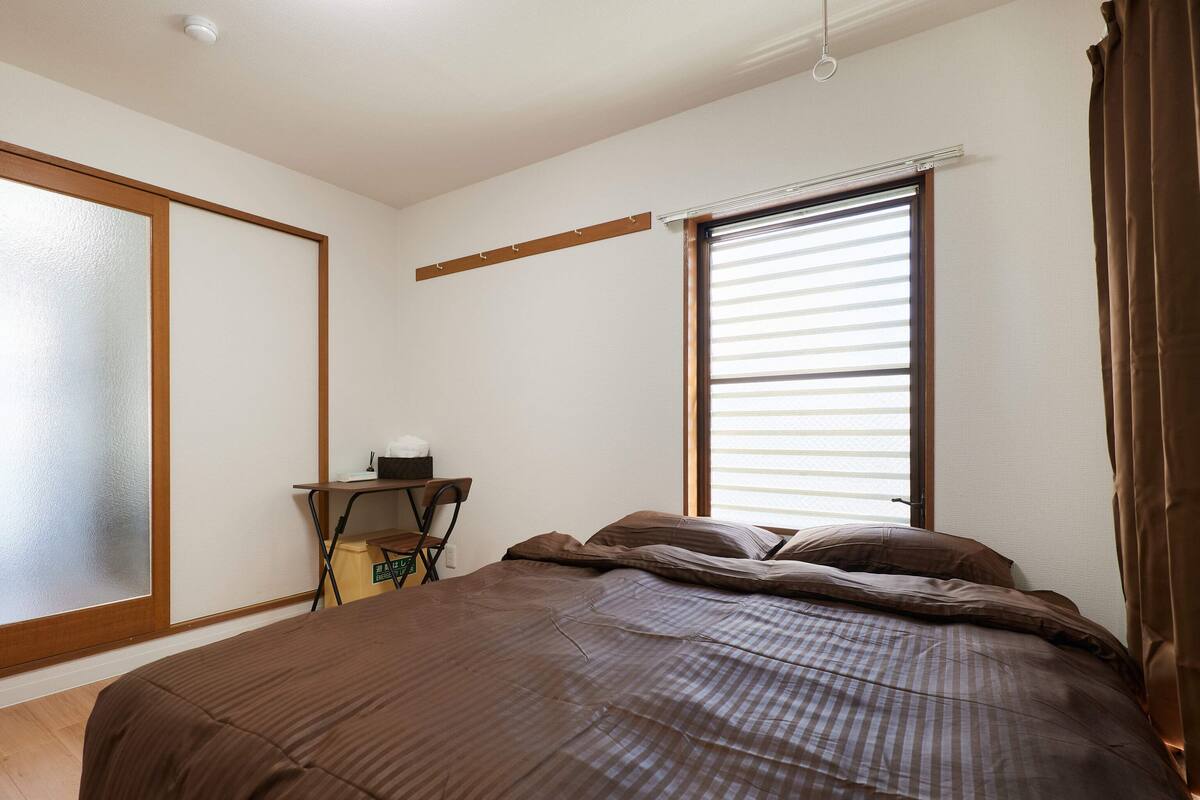 A bedroom with a bed, a desk, and a window with blinds.