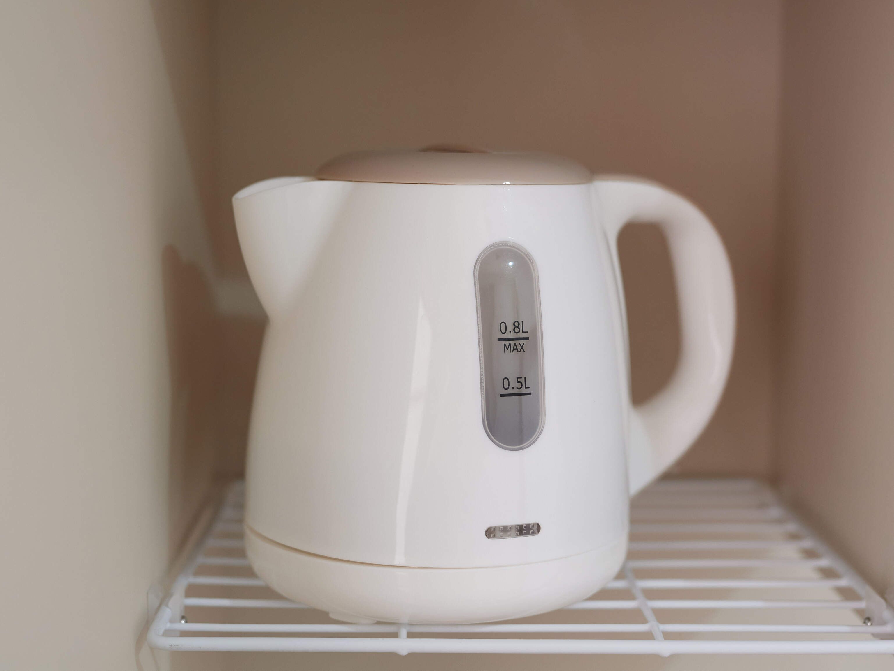 A white electric kettle with a digital display on a white shelf.