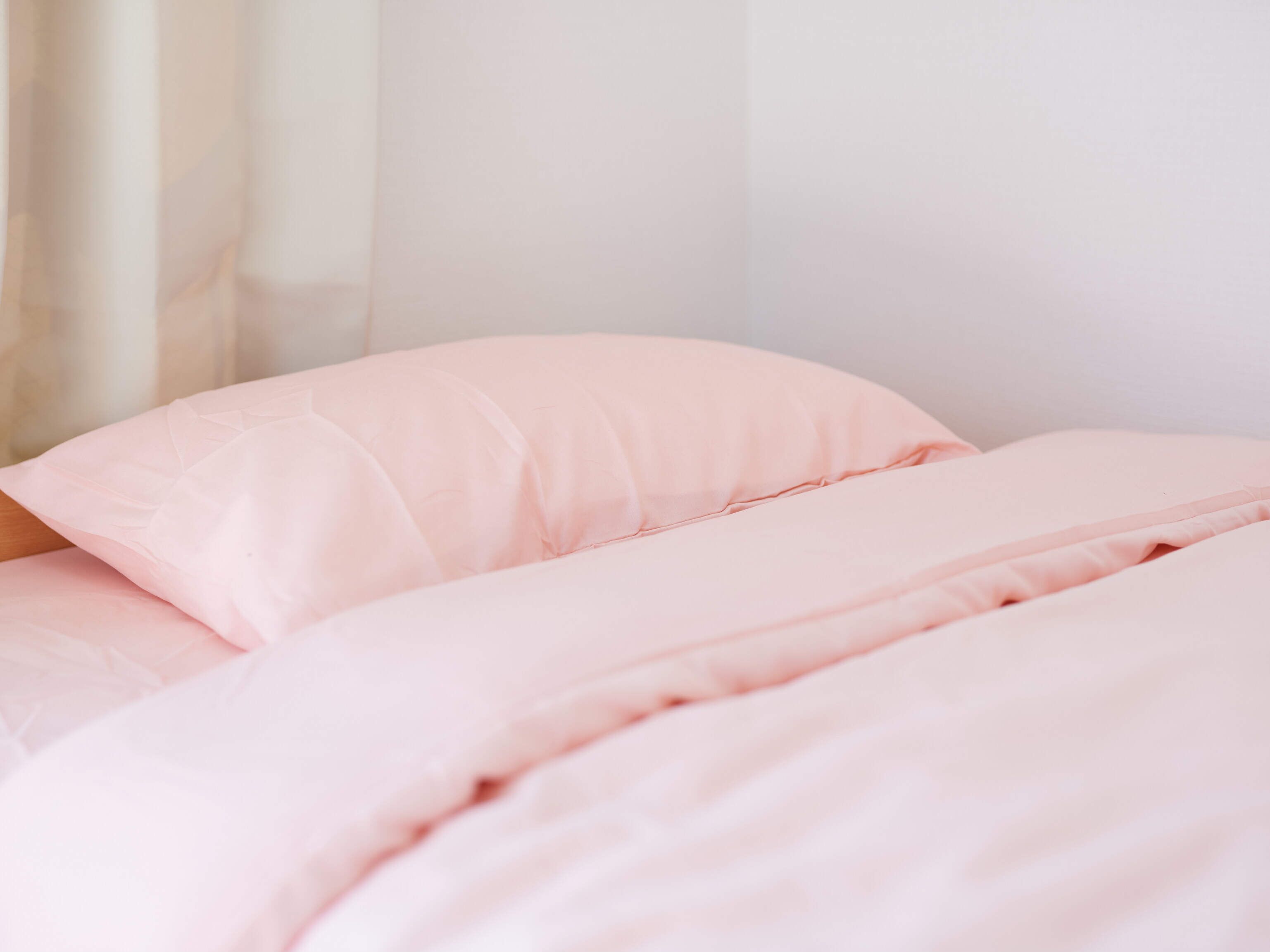 A bed with pink bedding and a white wall in the background.