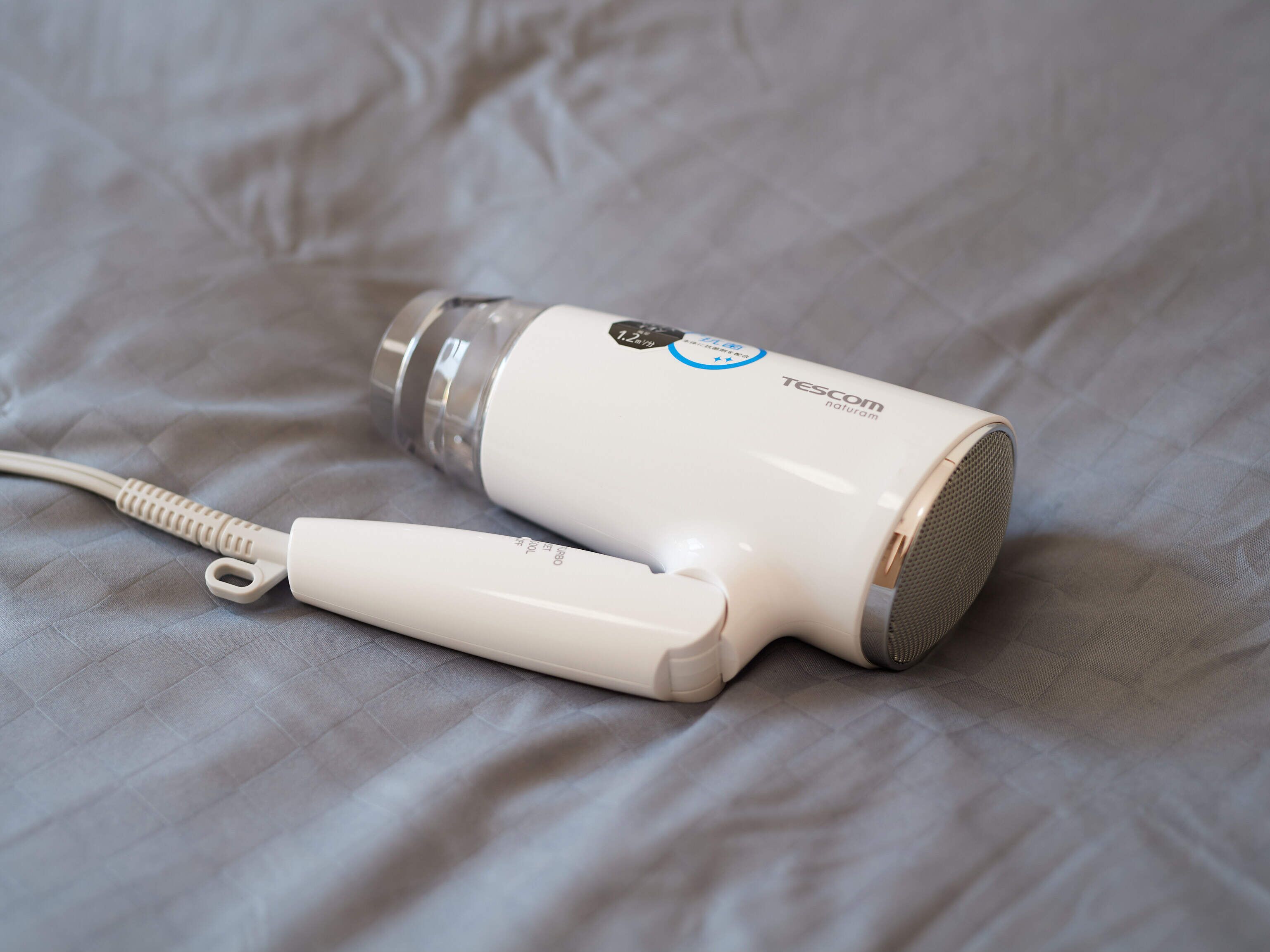 Um secador de cabelo branco com fio e um botão de energia sobre uma superfície de tecido texturizado.
