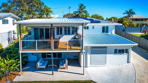 Una casa a due piani con un balcone, un garage e una zona relax all'aperto coperta.