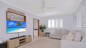 Un soggiorno con TV a schermo piatto, ventilatore a soffitto, divano e un cartello che recita 'BEACH HOUSE'.