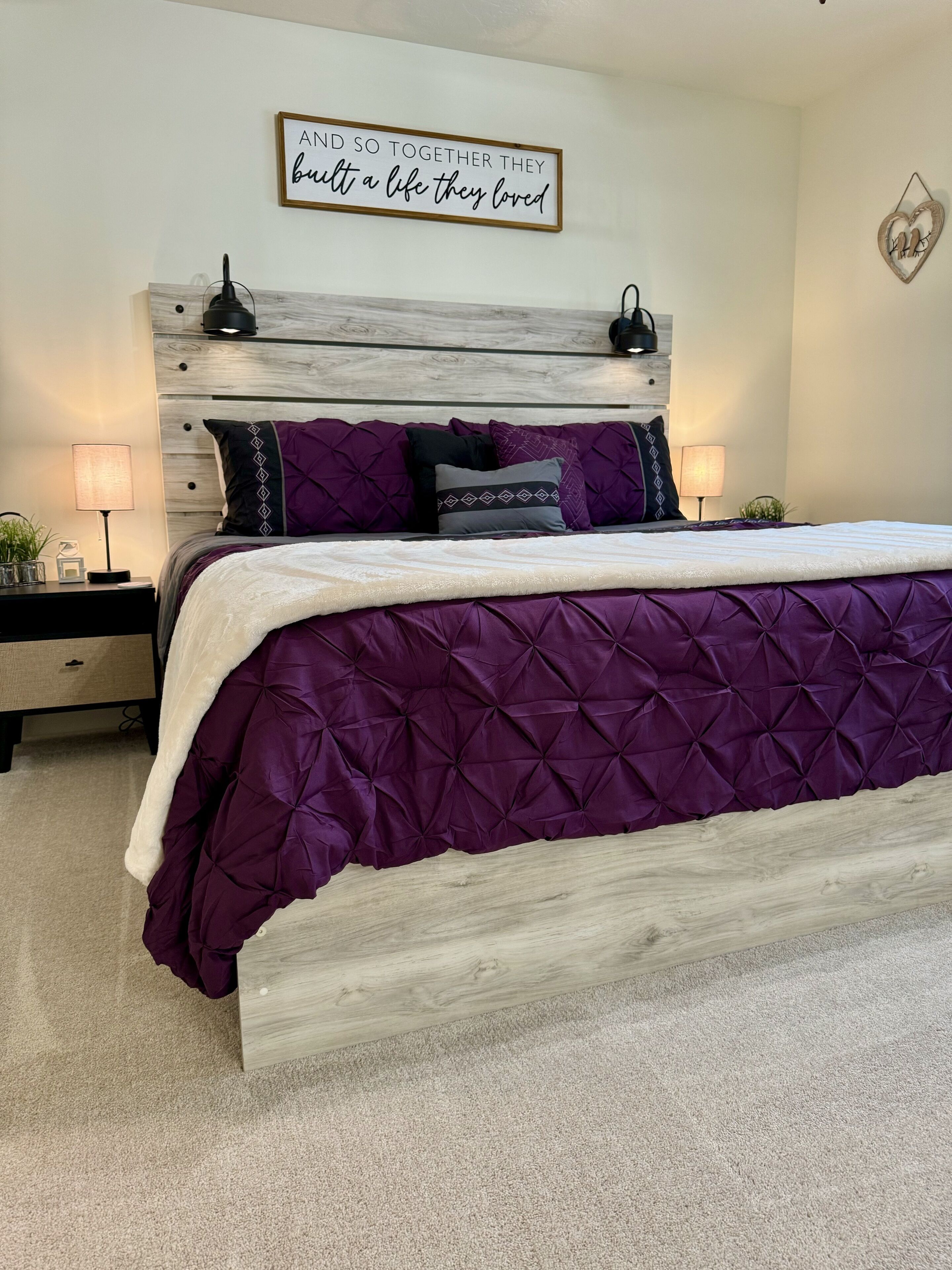 A bedroom with a wooden headboard, a purple quilted bedspread, and a motivational quote on the wall.