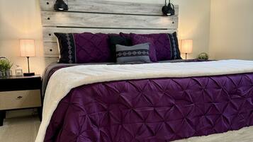A bedroom with a wooden headboard, a purple quilted bedspread, and a motivational quote on the wall.
