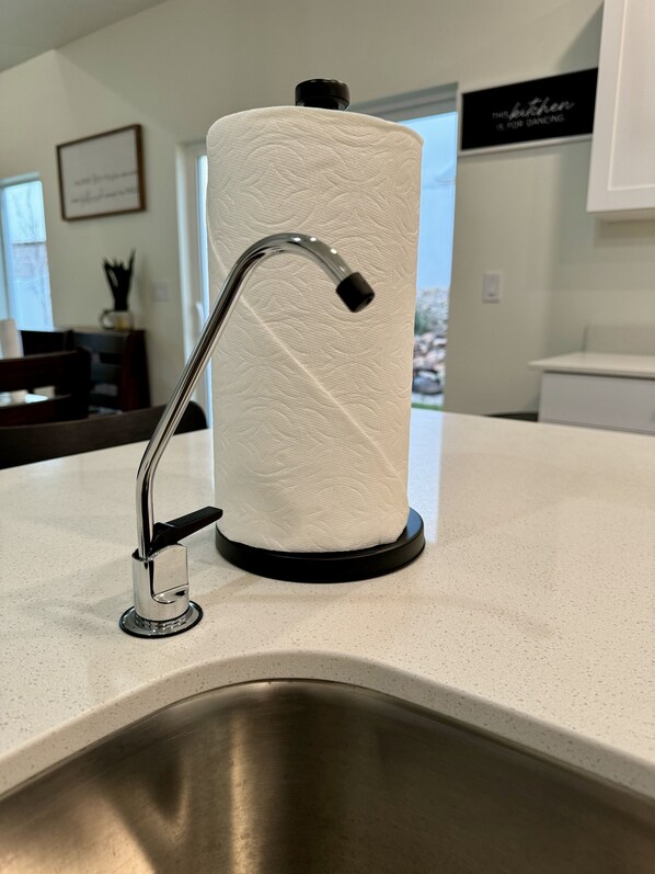 Una cocina con un lavamanos de acero inoxidable, un dispensador de toallas de papel y un cartel en la pared.