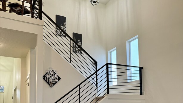 Un vaste salon comprenant un canapé d’angle gris, une table basse et un escalier avec une rampe noire menant à un niveau supérieur.