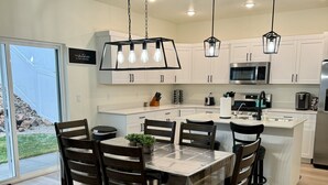 Une cuisine moderne avec des meubles blancs, des appareils en acier inoxydable et un coin repas comprenant des chaises en bois et une table en verre.