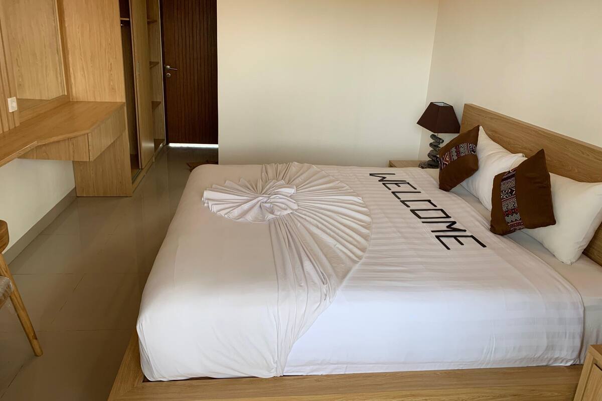 A neatly made bed with a 'WELCOME' sign, wooden headboard, and patterned pillows.