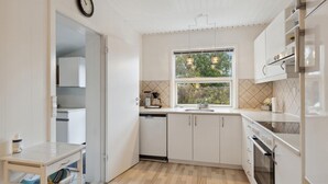 Een moderne keuken met witte kastjes, een vaatwasser, een oven en een raam met uitzicht op groen.