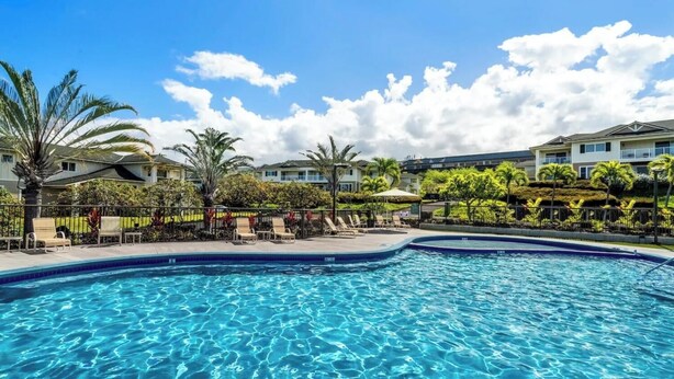 Piscina com espreguiçadeiras e palmeiras, cercada por edifícios.