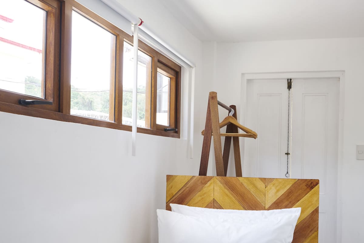 A neatly made bed with a patterned bedspread, a wooden headboard with a chevron design, and a wooden hanger rack against the wall.