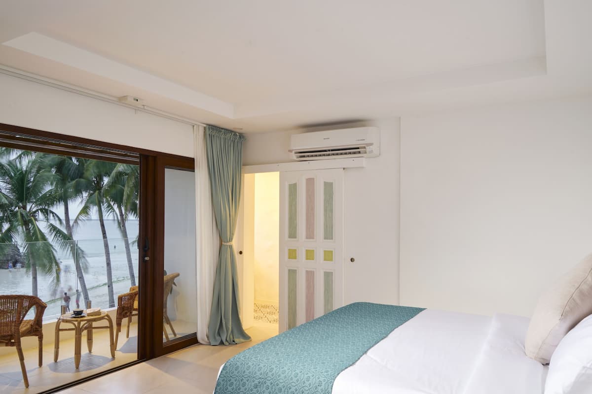 A bedroom with a bed, a window with a view of palm trees and the sea, and an air conditioning unit on the wall.