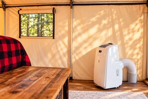 A tent interior with a table, a couch, a heater, and a window with a view of trees.