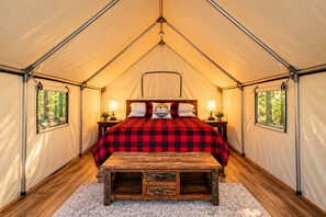 A tented room with a bed, bedside tables, and a wooden bench. - The Pioneer at Ozark Mountain Adventure Branson, MO Glamping (Branson)