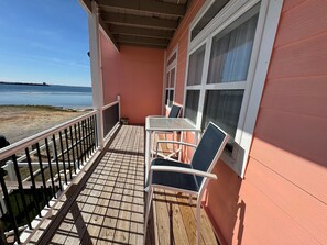 A balcony with a view of the sea, a table with chairs, and a window with curtains.