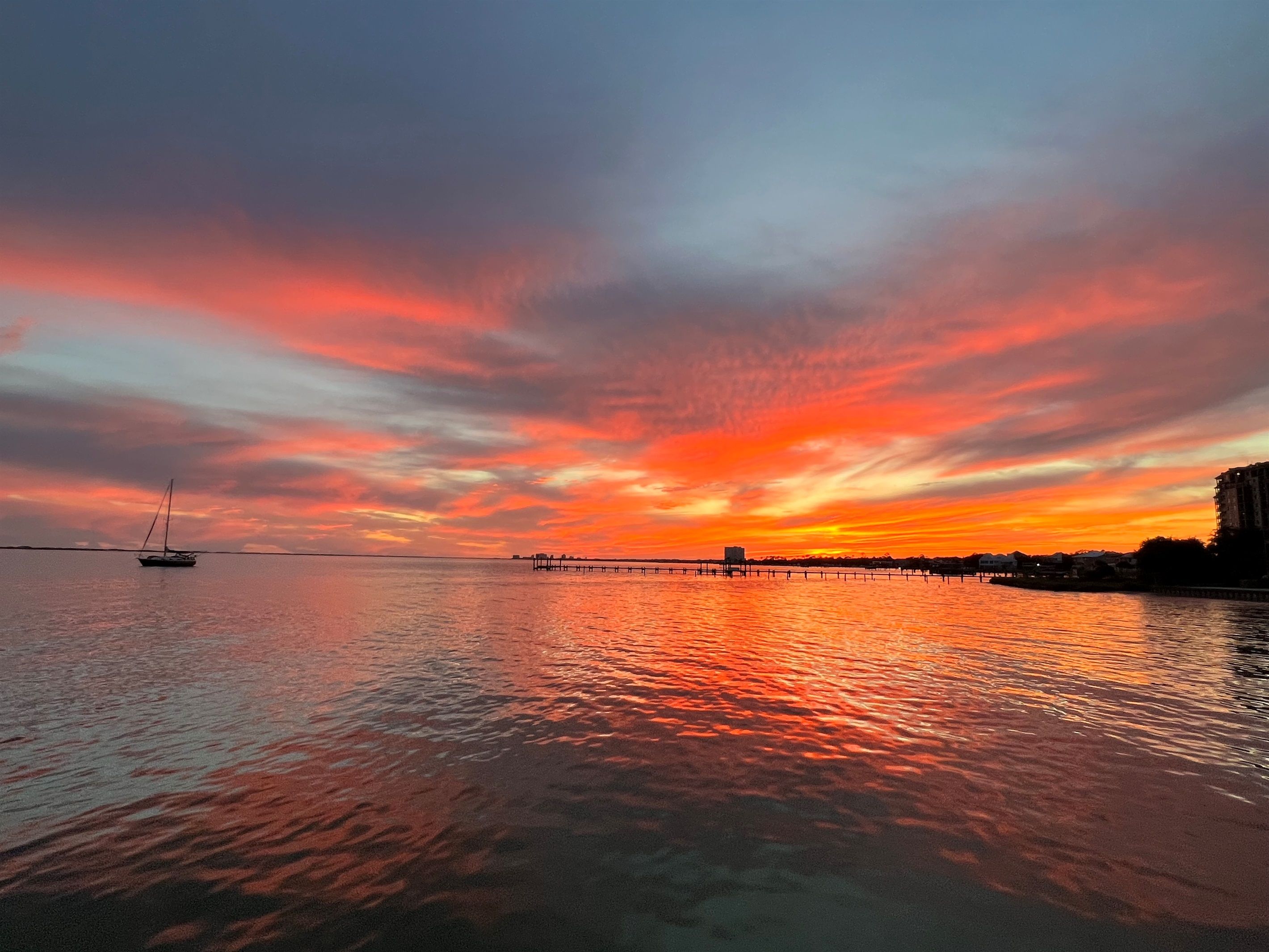 A sunset over a calm body of water with a dock and a sailboat.
