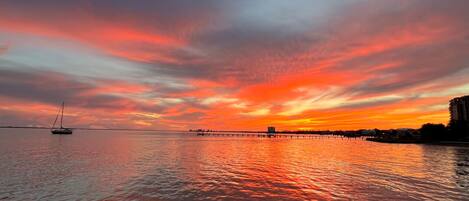 A sunset over a calm body of water with a dock and a sailboat.