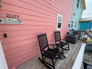 A pink building with the number 10129 and a welcome sign. There are two rocking chairs on the porch.