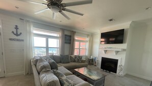 Una sala de estar con un sofá modular, una chimenea, un televisor de pantalla plana y un ventilador de techo.