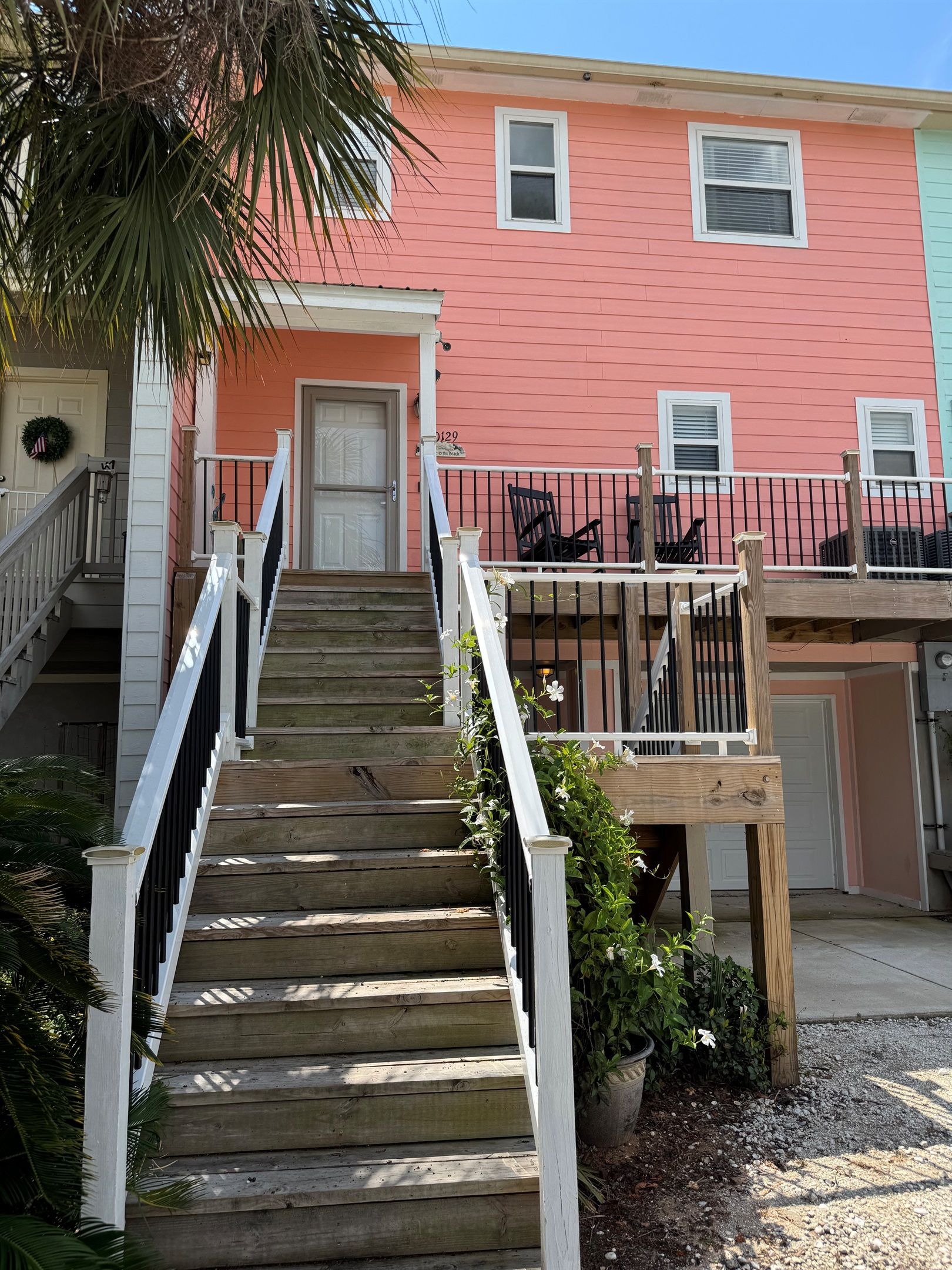 A wooden staircase leading to a pink building with white railings and a small porch area.