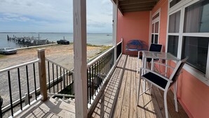 Terraza de madera con barandilla, banco y mesa, con vista a un puerto deportivo con barcos y un muelle.