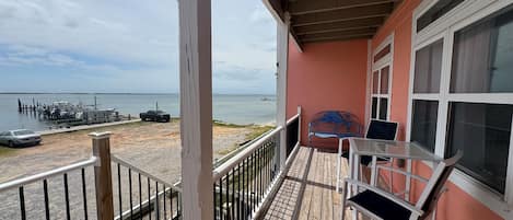 Terraza de madera con barandilla, banco y mesa, con vista a un puerto deportivo con barcos y un muelle.