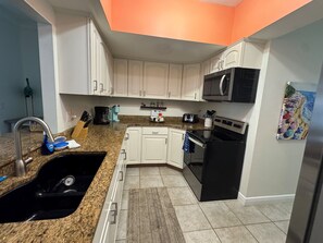 Una cocina con armarios blancos, un refrigerador negro, un microondas y una cafetera.