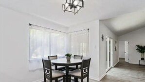 Un coin repas avec une table ronde et quatre chaises, une plante en pot posée sur la table et un lustre au-dessus.