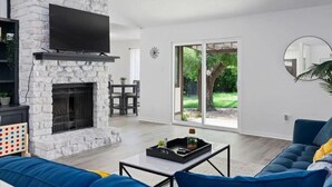 Un salon moderne doté d’une cheminée en pierre, d’un téléviseur à écran plat et d’une grande porte-fenêtre coulissante donnant sur un jardin.