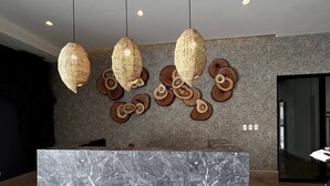Uma área de recepção com balcão de mármore, luminárias pendentes trançadas e jogos de apoio de madeira na parede.