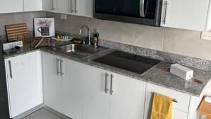 Uma cozinha moderna com armários brancos, bancada de granito, pia de aço inoxidável e micro-ondas embutido.