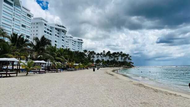 Uma praia com uma fileira de hotéis brancos, palmeiras e uma orla arenosa.