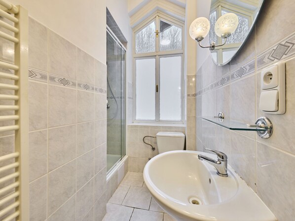 A bathroom with a white sink, a glass shower enclosure, a toilet, and a window with a view of trees.