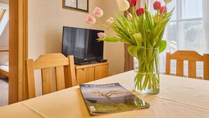 A room with a wooden table, a glass vase with tulips, a framed certificate on the wall, and a television on a wooden stand. - Stříbrný pramen by Interhome (Janské Lázně)